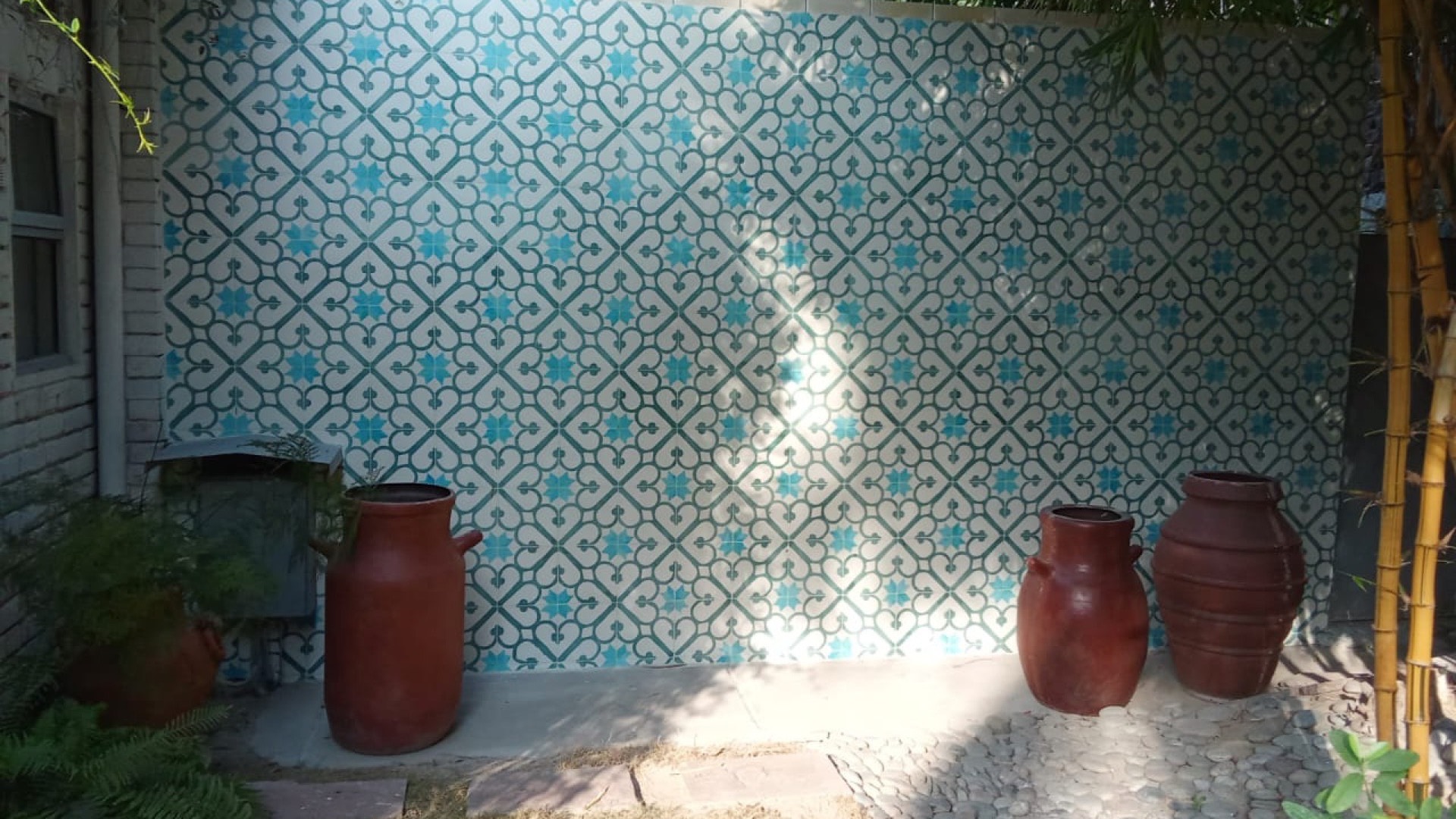 A garden courtyard wall clad in teal and white patterned TARSEEM tile
